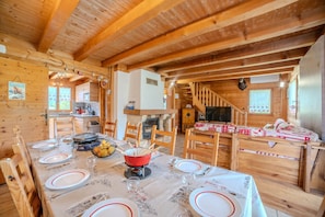 L’intérieur d’un chalet en bois comprend une table à manger pour quatre personnes, une cheminée et un escalier menant à un autre niveau.