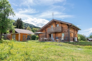 Une cabane en bois dotée d’un balcon, entourée d’un champ verdoyant et d’arbres.