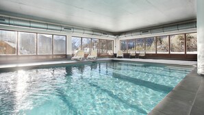Ein Hallenbad mit klarem Wasser, umgeben von Fenstern mit Blick auf die Berge.