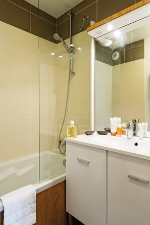 A modern bathroom with a glass-enclosed shower, a white vanity with a mirror, and toiletries on the counter. - Navette gratuite pour la station + Accès Piscine (Pralognan-La-Vanoise)
