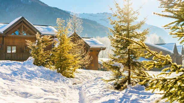 Una cabana de fusta amb un teulat cobert de neu i un paisatge de muntanya de fons.