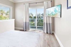 A bedroom with a bed, a sliding glass door to a balcony, and a TV mounted on the wall. - Wave on Wave by Stay on 30a (Seacrest)