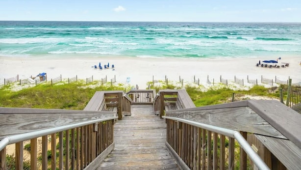 Una passerella in legno che conduce a una spiaggia, con una recinzione e alcune persone in lontananza.