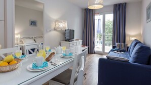 Una habitación de hotel moderna con zona de comedor, sofá y balcón con cortinas.
