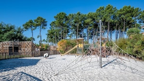 Un parque infantil con estructuras para escalar y un tobogán, rodeado de árboles y una valla de madera.