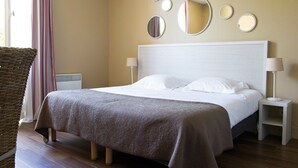Una camera d'albergo con un letto grande, un comodino con una lampada, uno specchio a parete e una poltrona in vimini.