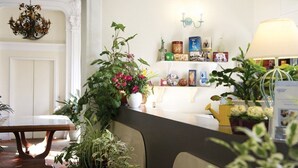 Un'area reception con una scrivania in legno, piante in vaso, un lampadario e una mensola a parete con diversi oggetti.