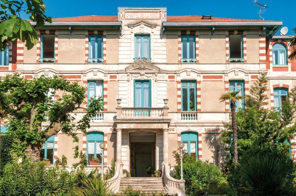 Un edificio histórico con una entrada central, varias ventanas con contraventanas y una fachada simétrica.
