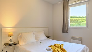 A hotel room with a bed, a bedside lamp, a window with curtains, and a view of greenery outside.