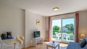 A room with a sofa, a coffee maker, a TV, and a table. - Appartement spacieux | Accès piscine (PLESCOP)