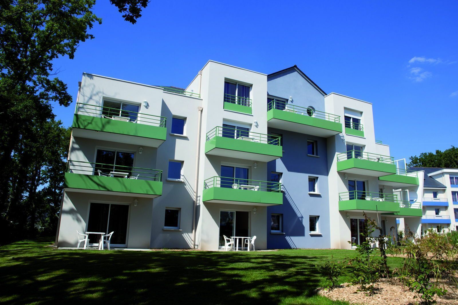 Un edificio residencial de varios pisos con balcones, césped y mobiliario exterior.
