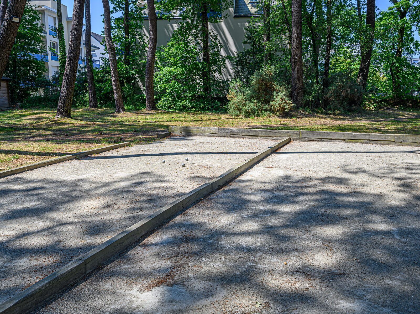 An outdoor area with a concrete surface, surrounded by trees and a building in the background.