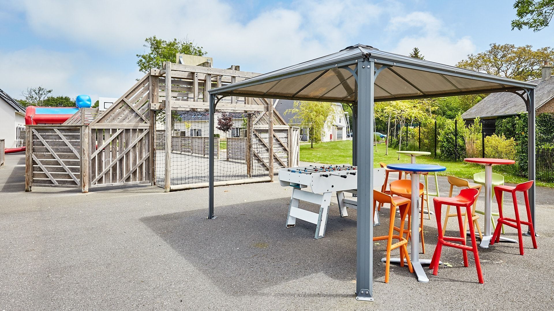 A playground with a climbing structure, a foosball table, and colorful chairs.