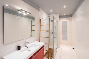 Ein modernes Badezimmer mit einem weißen Waschbecken, einem großen Spiegel und einer Duschkabine aus Glas.