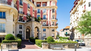 Edifici de diverses plantes amb balcons, una entrada central i un jardí ben cuidat.