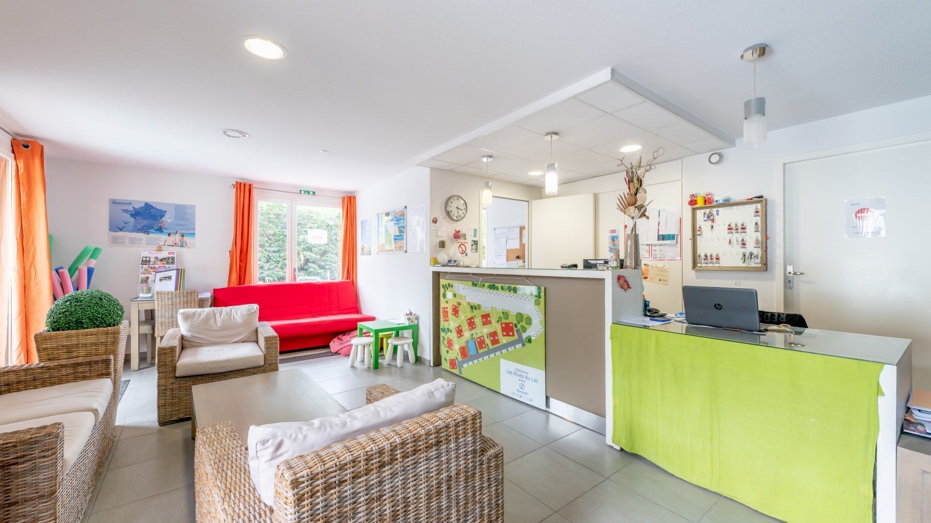 A bright and welcoming reception area with a green counter, wicker furniture, and a red sofa.