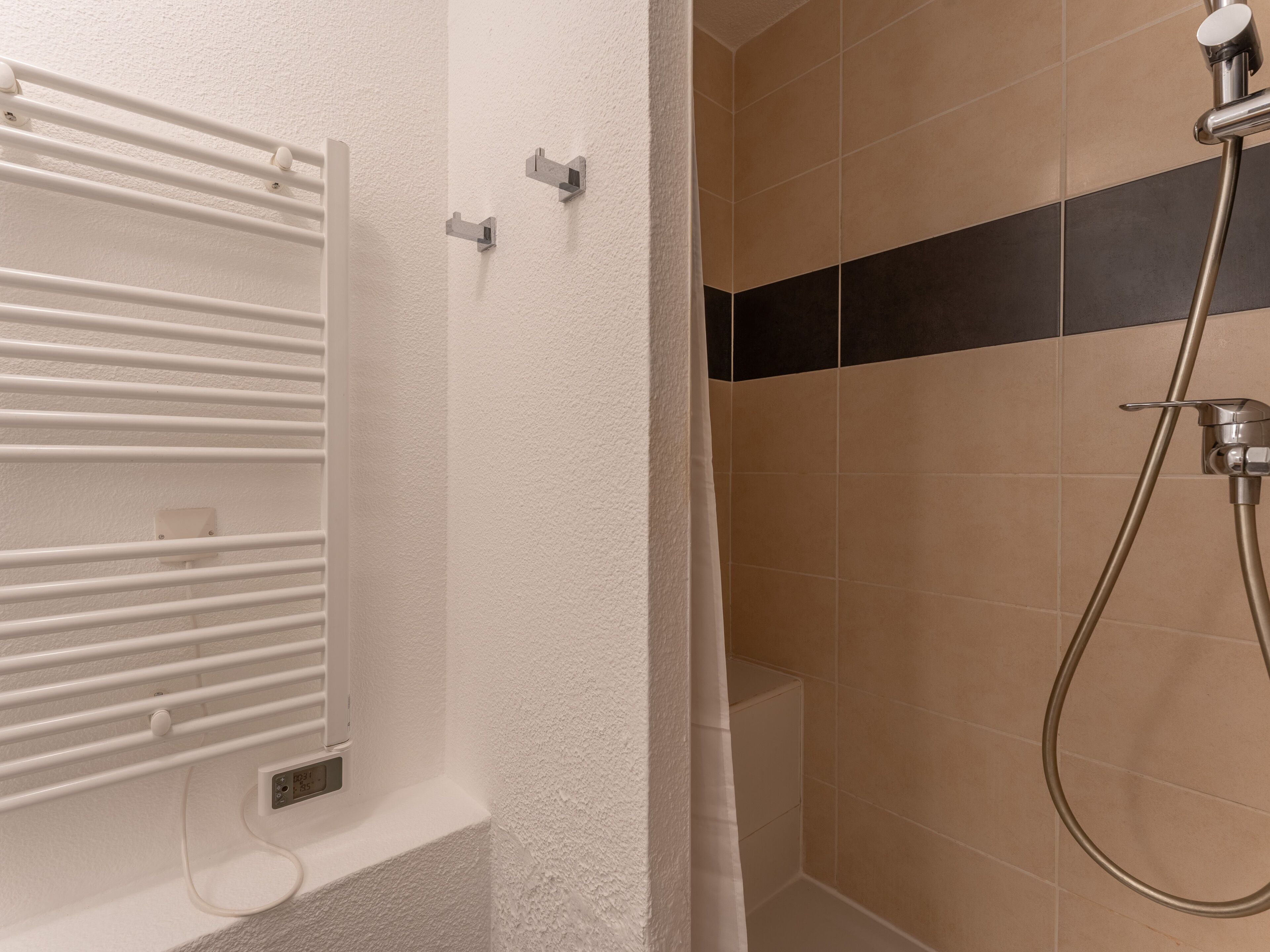 A bathroom with a white bathtub, a shower with a handheld showerhead, and a towel rack.