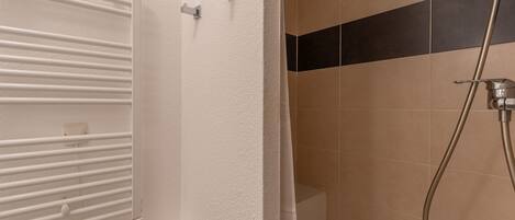 A bathroom with a white bathtub, a shower with a handheld showerhead, and a towel rack.