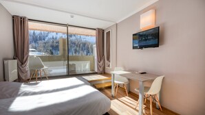 Une chambre d’hôtel moderne, dotée d’un grand lit, d’un bureau avec une chaise, d’une télévision et offrant une vue sur un paysage enneigé grâce à la porte vitrée.