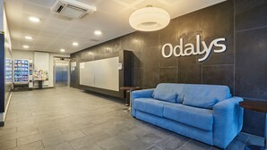 Un espace d’accueil avec un canapé bleu, un distributeur automatique et une enseigne fixée au mur portant l’inscription « Odalys ».