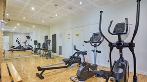 Une salle de sport équipée de divers appareils d’exercice, dotée d’un plancher en bois et d’un grand miroir.