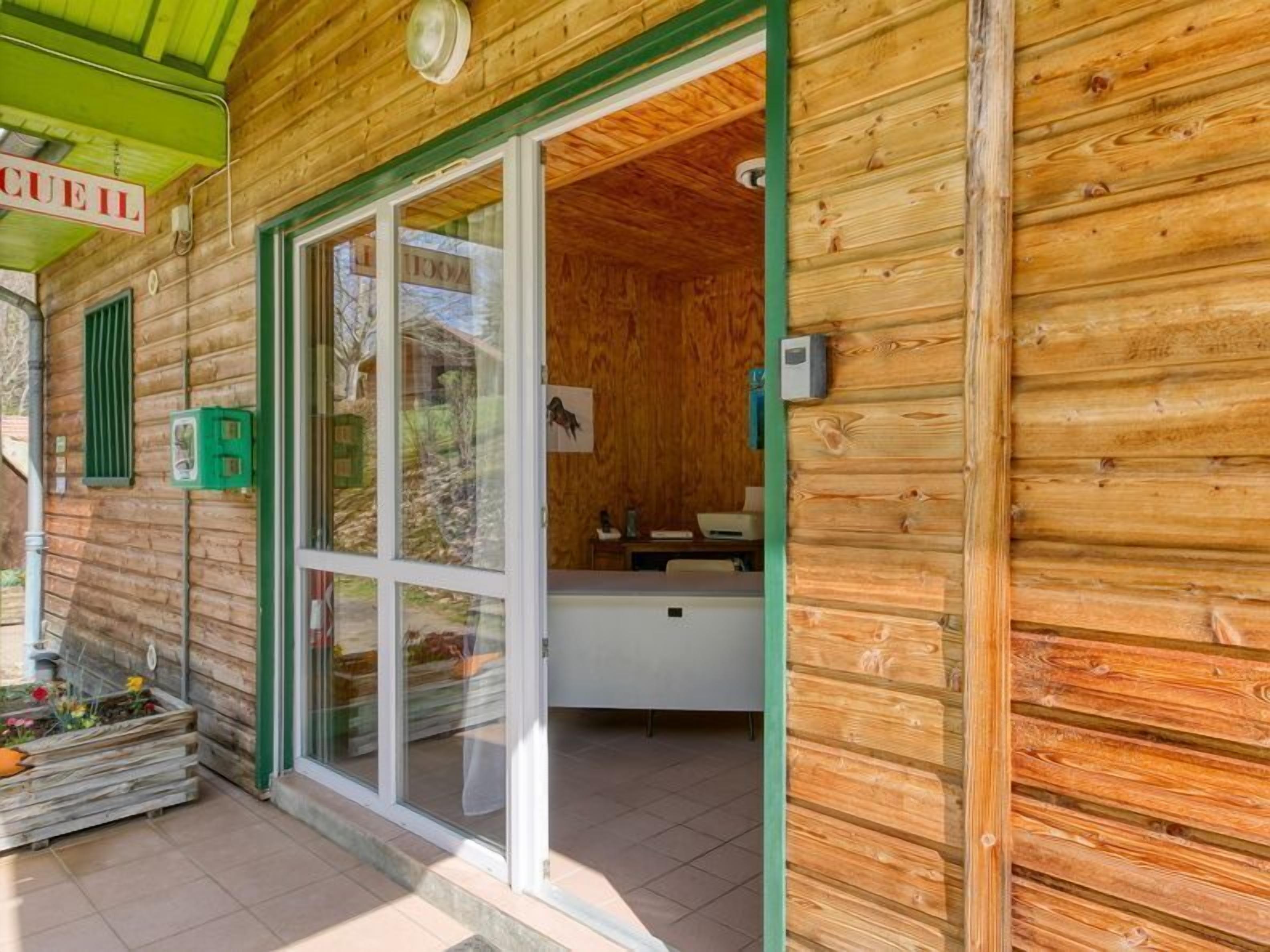 Eine Holzhütte mit Glastür, einer kleinen Küchenzeile und einem grünen Vordach.