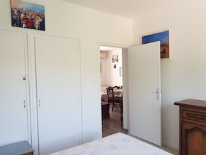 Ein Zimmer mit weißen Wänden, einem Bett, einem Holzschrank und einem Essbereich im Hintergrund.