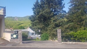 A gated entrance with a sign, a building with a balcony, and a mountainous backdrop.