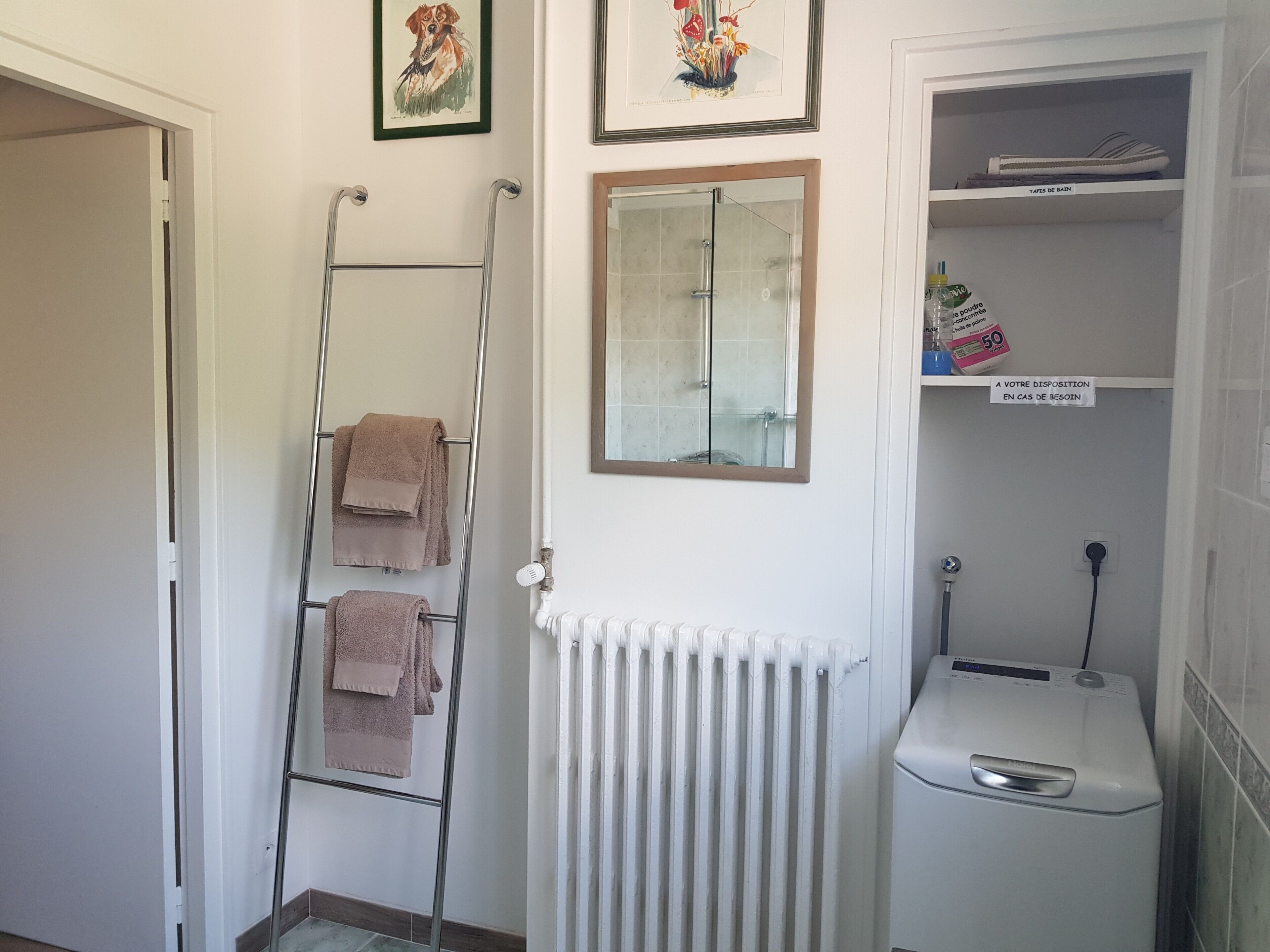 A bathroom with a towel rack, a radiator, a mirror, and a shelf with toiletries.