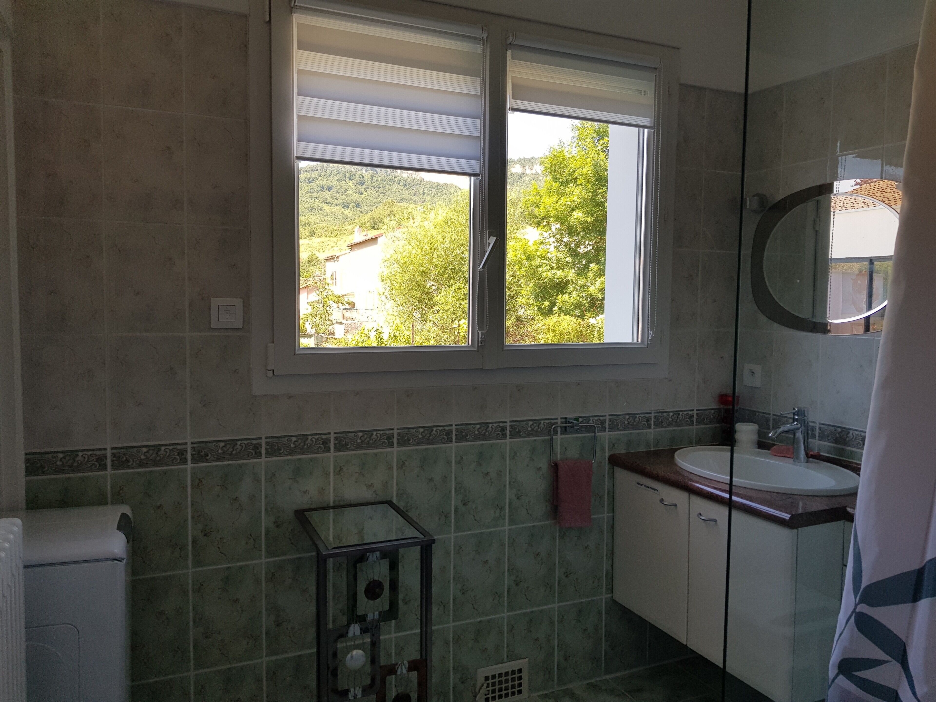 Une salle de bain avec une fenêtre, un lavabo, un miroir et un radiateur.