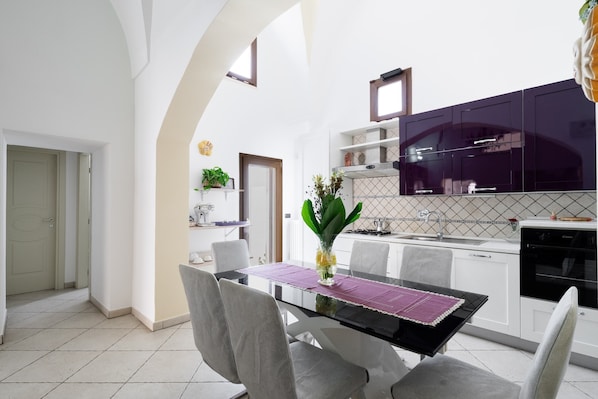 A modern kitchen with white cabinets, a black countertop, and a purple placemat on the dining table.