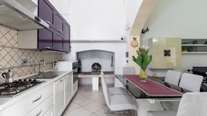 Een moderne keuken met een gasfornuis, witte kasten, een eethoek met een tafel en stoelen, en een open haard.