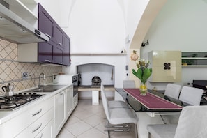 A modern kitchen with a gas stove, white cabinets, a dining area with a table and chairs, and a fireplace.