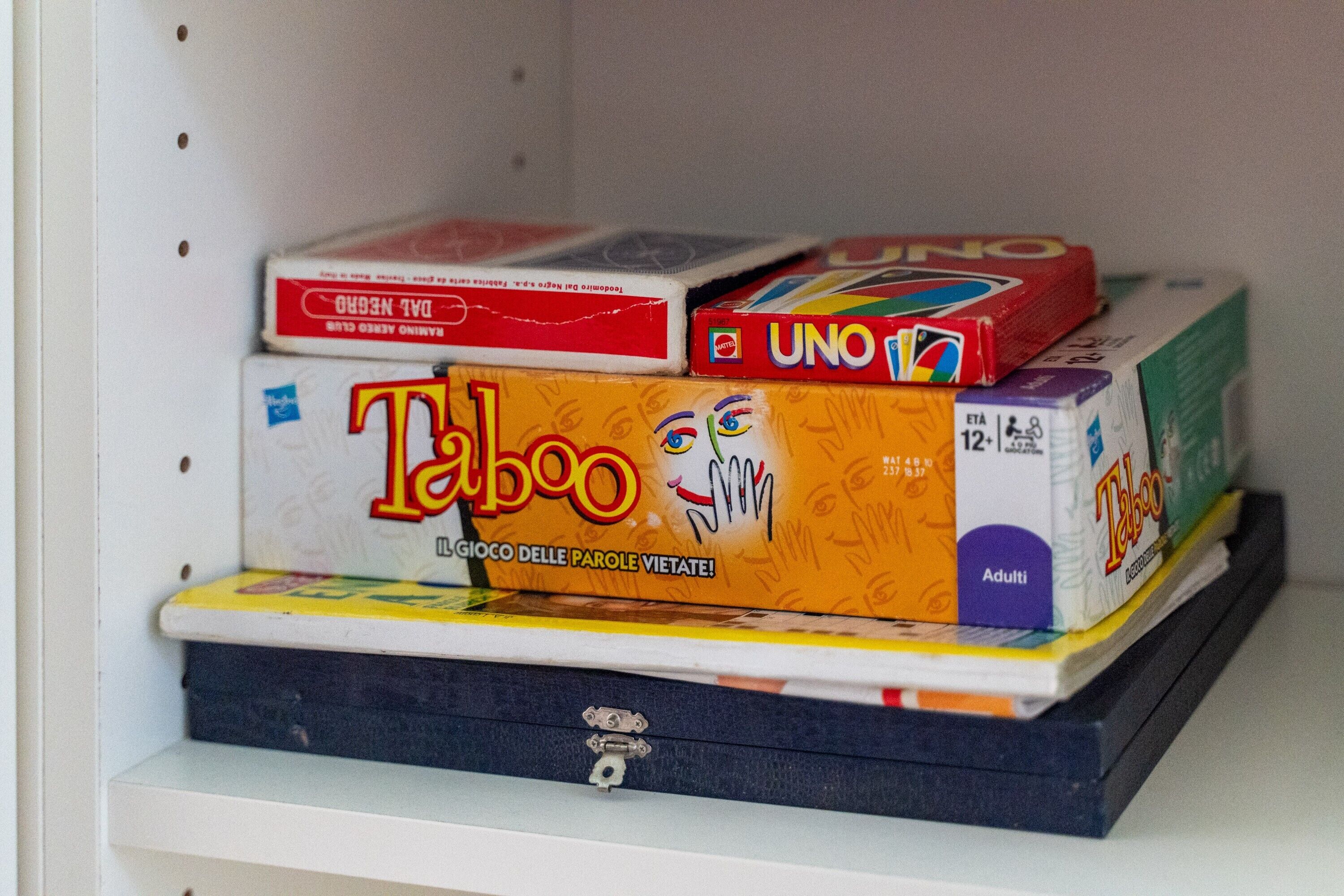 Una estantería con varios juegos de mesa, incluyendo UNO y Taboo.
