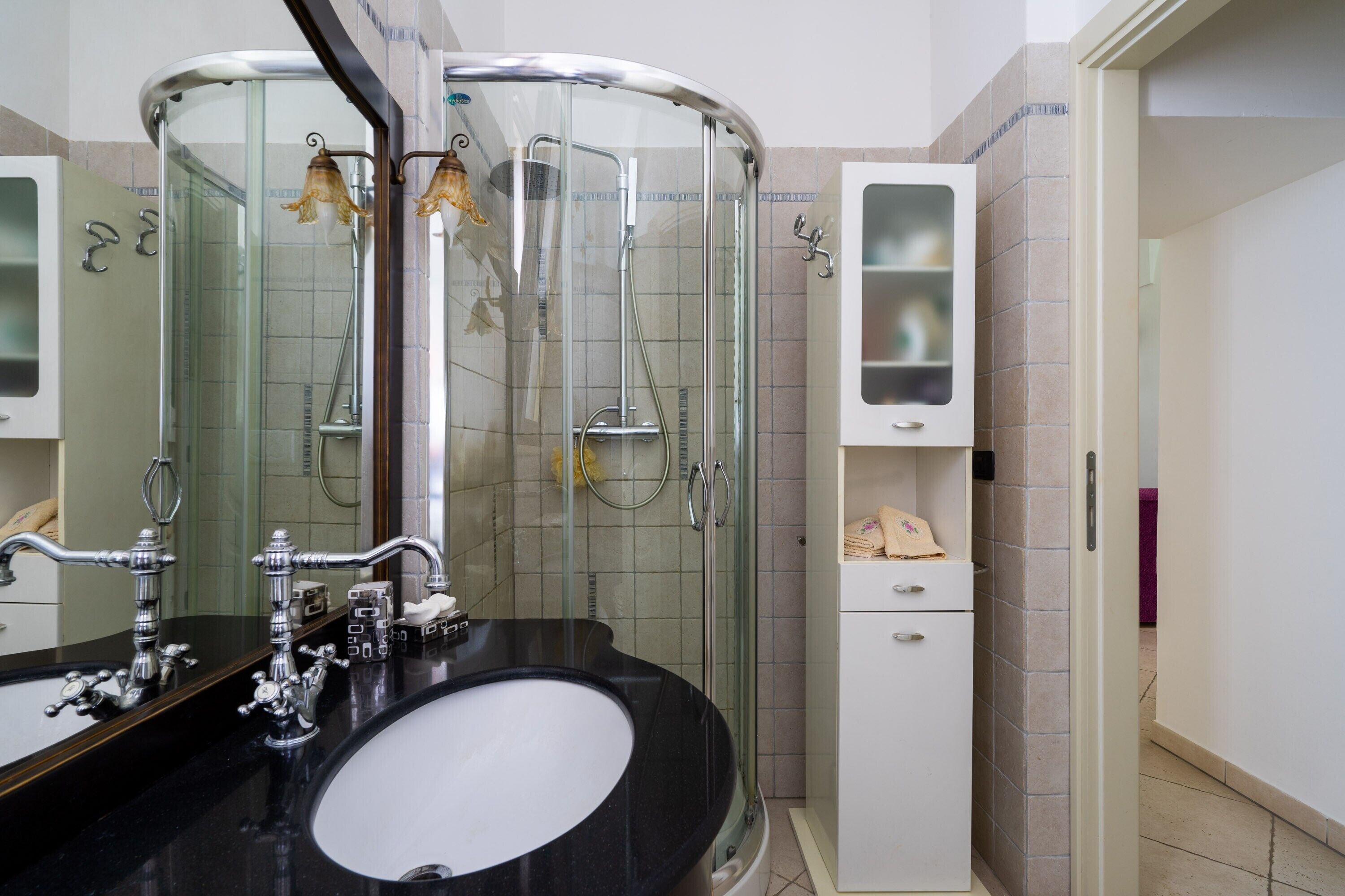 Een moderne badkamer met een zwart wastafel, een douche met glazen wanden en een wit kastje met lades.