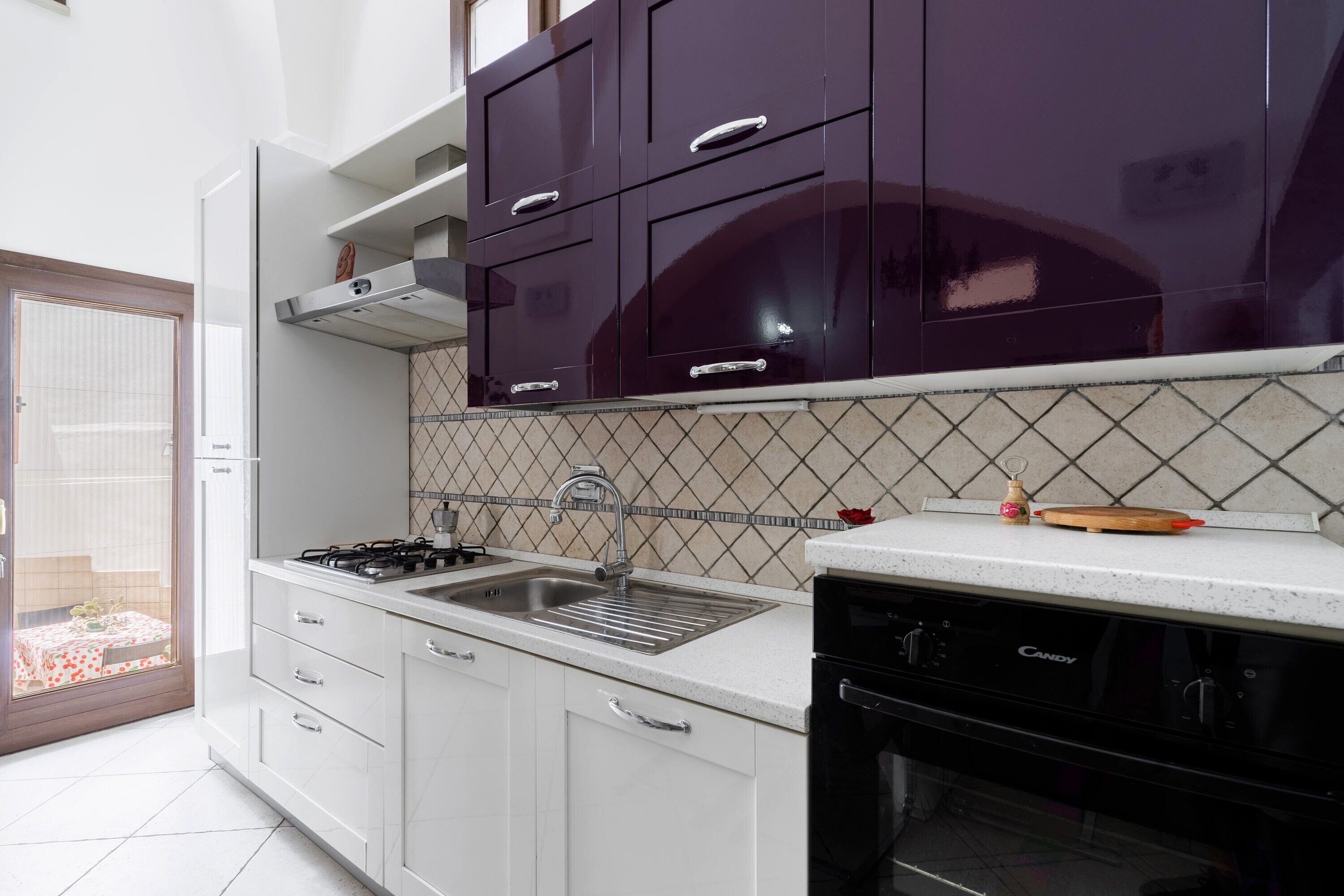 Une cuisine avec des meubles blancs, une cuisinière noire et un dosseret carrelé.