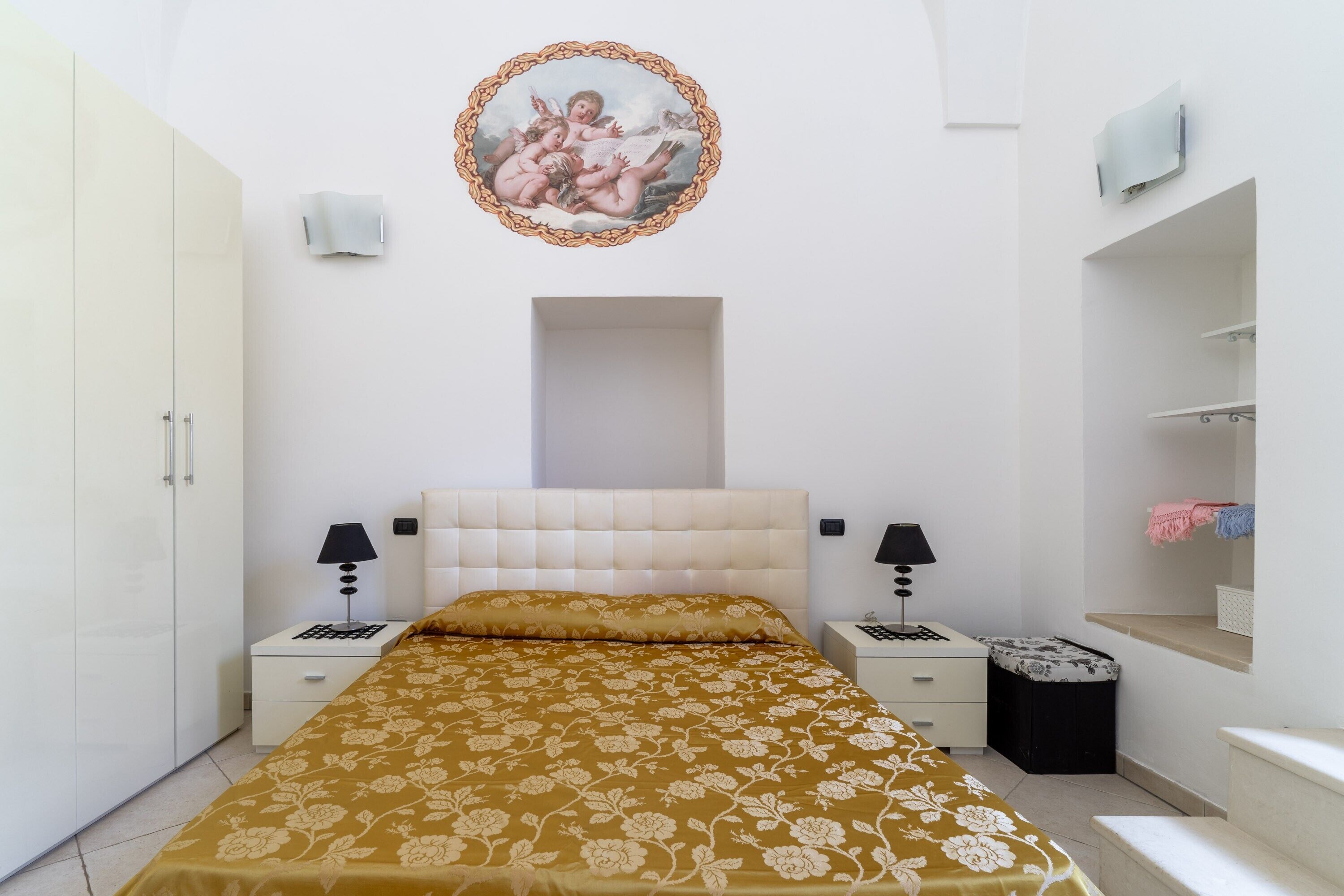 A bedroom with a bed, nightstands, a wardrobe, a painting, and a small stool.