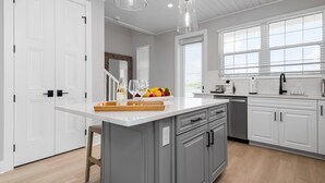 A modern kitchen with white cabinetry, a central island with a fruit bowl, and pendant lighting.