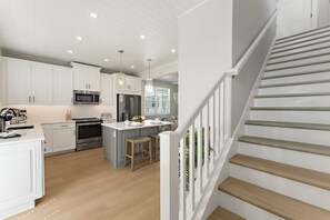 Una cocina moderna con armarios blancos, electrodomésticos de acero inoxidable y una isla de madera con taburetes.