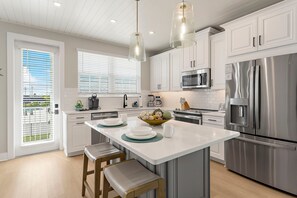 A modern kitchen with white cabinetry, stainless steel appliances, and a central island with stools.