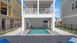 Un edificio a due piani con un balcone, una piscina e una zona relax con poltrone prendisole.