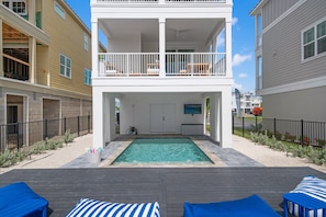 Ein zweigeschossiges Gebäude mit Balkon, Schwimmbecken und einer Terrasse mit Liegestühlen.