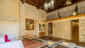 Un interior rústico con paredes de piedra vista, techo de madera, comedor con mesa y sillas, y una escalera que sube a un nivel superior.