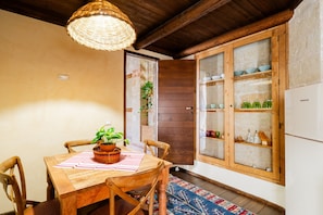 A wooden dining table with chairs, a woven light fixture, a potted plant, and a cabinet with glass doors.