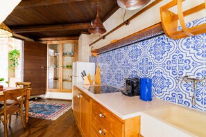 A kitchen with wooden cabinets, a white countertop, a blue and white patterned backsplash, and a hanging copper light fixture.