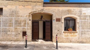 Un edificio de piedra con una gran entrada en arco, un pequeño ventanal con una planta en maceta y un letrero con el número 2.