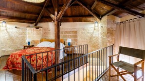 Una habitación rústica con techo de madera, una cama con colcha roja, un banco y paredes de piedra.