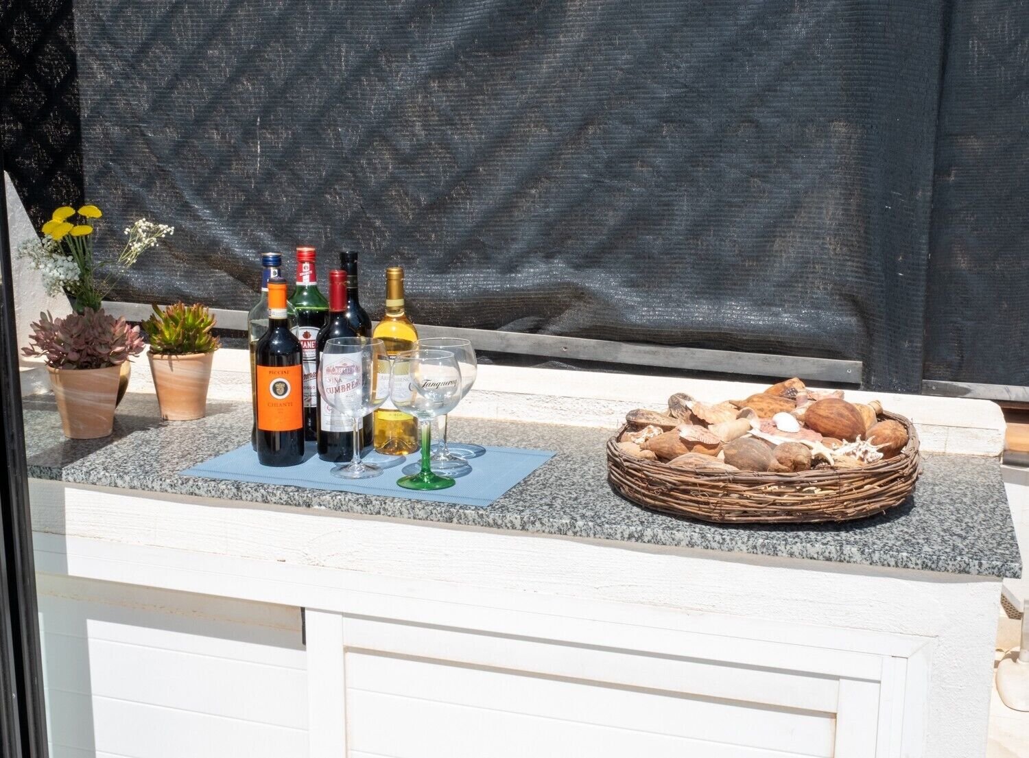 A bar area with bottles of wine, glasses, and a basket of nuts.