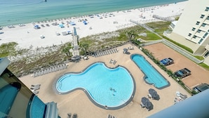 A pool area with multiple swimming pools, a beach with umbrellas and lounge chairs, and a view of the ocean. - Palacio 704 | Beachfront, Resort Amenities | My Beach Getaways (Pensacola)