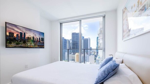 A hotel room with a large bed, a cityscape view through a window, and a painting on the wall. - Skyline View Condo with Pool (Miami)